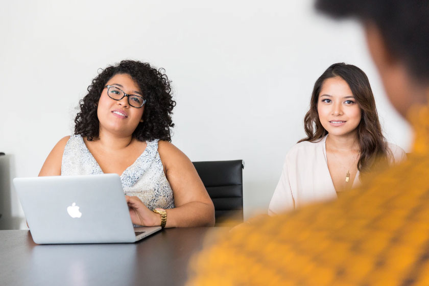 Two women sat at a table with a laptop