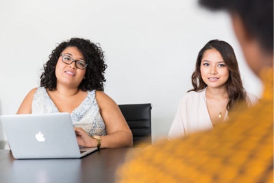 Two women sat at a table with a laptop